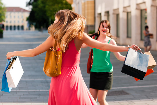 两个女人是朋友，拿着五颜六色的购物袋在市中心购物，她们走在街上玩得很开心