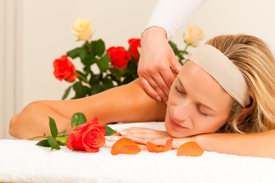 在以玫瑰为背景的spa环境中享受健康背部按摩的女士，她非常放松（特写）