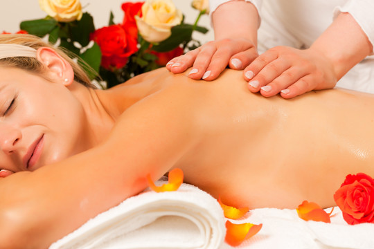 在以玫瑰为背景的spa环境中享受健康背部按摩的女士，她非常放松（特写）