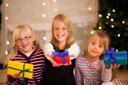 三个女孩在圣诞树前拿着礼物