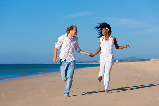 一对黑人妇女和一对白人男子在度假时沿着海滩散步和奔跑
