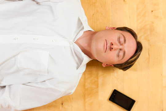他闭着眼睛躺在家里的地板上，旁边放着一部电话