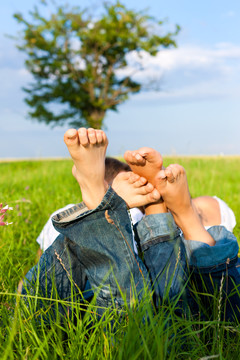 一对幸福的夫妇在夏天躺在草地上，只看到脚