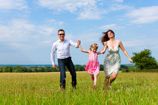 快乐的家庭-母亲，父亲，孩子-在夏天在绿色的草地上奔跑