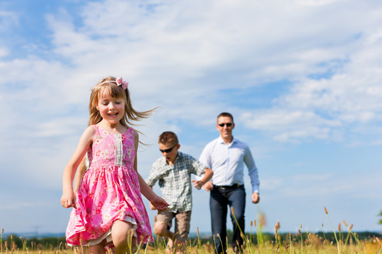 快乐的家庭-父亲，孩子们-在蓝天下的草地上玩耍