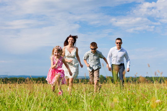 快乐的家庭-母亲，父亲，孩子们-在蓝天下的草地上玩耍