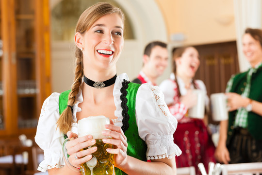 年轻人在传统的巴伐利亚餐馆或酒吧里，一个女人正站在啤酒史坦面前，一群人在后面