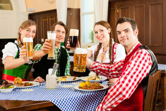 年轻人在传统的巴伐利亚餐厅或酒吧吃午餐或晚餐，他们对着镜头敬酒