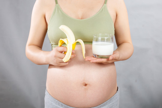 孕妇手上拿着一根香蕉和端着牛奶