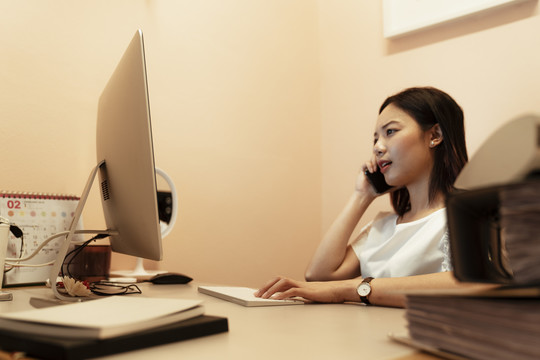 一个严肃的女人，一边打电话一边用电脑联系办公室的顾客。