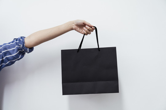 女人手拿黑色购物纸袋，一只手孤立在白色背景上。