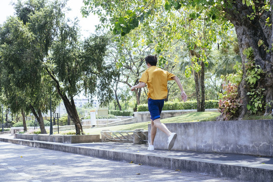 穿着黄色t恤和蓝色裤子的男孩在绿色公园里跑步。