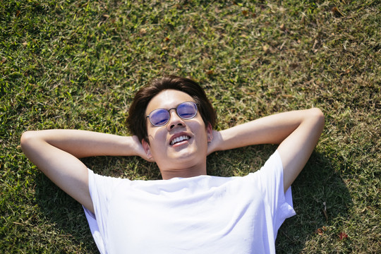 中等特写镜头黑发男子穿着白色t恤和眼镜躺在阳光下的领域。