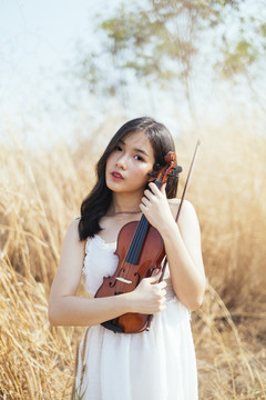 白衣女子站在草原上拉着漂亮的小提琴。