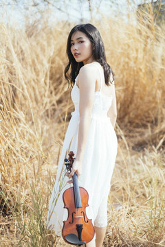 穿着白裙子的漂亮小提琴手走在草地上，拉着小提琴。