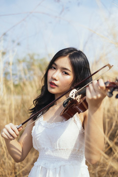 白衣黑发女子在风和日丽的草原上拉小提琴。