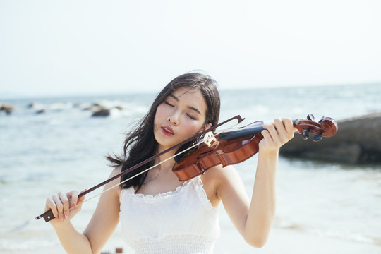卷曲的长发女人在风吹的日子里和岩石在海上拉小提琴。