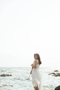 长发白衣女子胸前放着小提琴，站在风和日丽的海边。