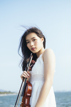 小提琴手白衣女子站在阳光下的肖像照。