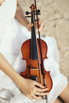 沙滩上白色连衣裙女人腿上的小提琴剪短图像，垂直。