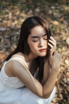 美丽的年轻女子穿着优雅的白裙闭上眼睛，坐在森林里。