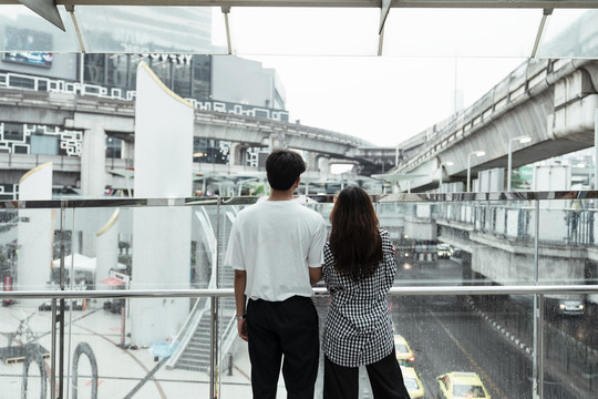 一对年轻夫妇站在城市的天桥上，看着大楼和道路。