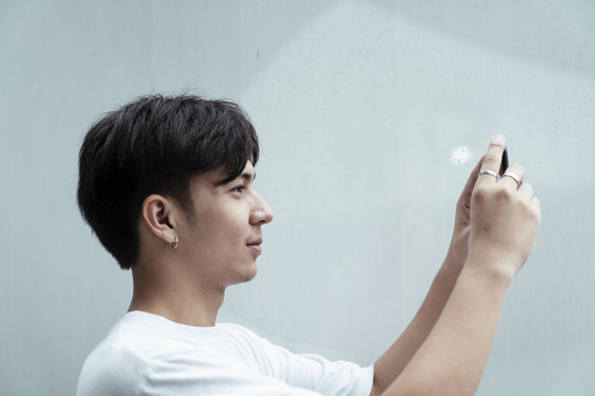 黑发小伙穿着白色t恤站在墙前，举着智能手机拍照。