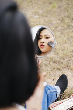 亚洲小女孩在便携式小镜子上用腮红刷脸的特写镜头。