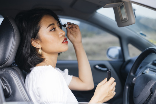 一位年轻的泰国妇女在匆忙的情况下化妆，在车里照镜子。