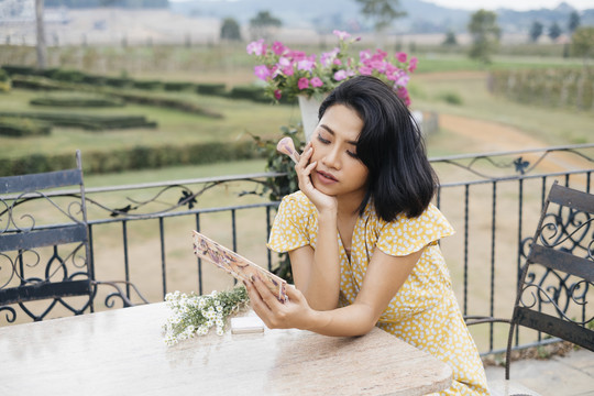 一个亚洲女人坐在乡下的椅子上，手里拿着刷子，看着化妆柜里的镜子。