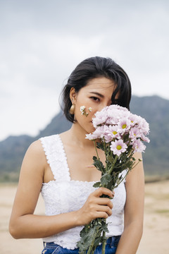 身穿白衬衫和蓝色牛仔裤的性感亚洲女子手持白色花束，站在乡间田野上的肖像。