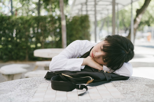 留着辫子和流苏头发的女学生在公园里的大理石桌旁睡觉，等待她的父母。