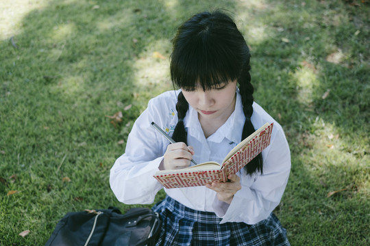 留着辫子和流苏头发的女学生坐在地上写作业本。