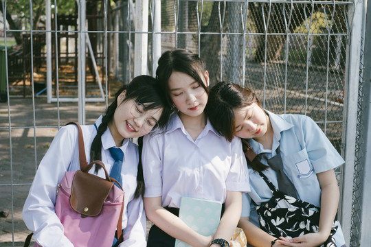 三个穿着不同制服的美丽的亚泰学生在休息时间在公园休息或睡觉。