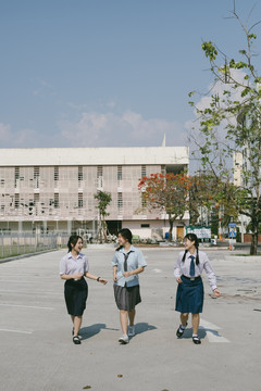 三个穿着不同制服的美丽的亚泰学生一起在学校户外散步。