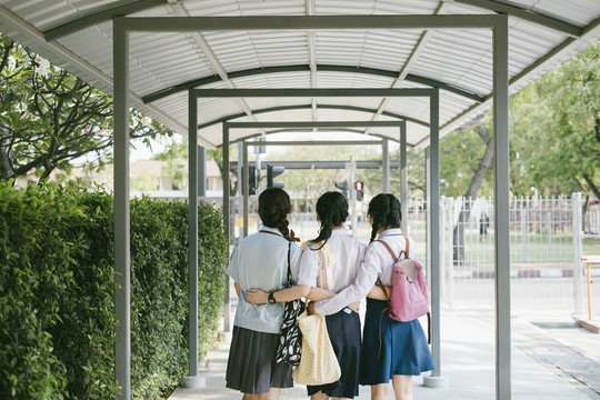 后视图-三个穿着不同制服的美丽亚泰学生放学后走出学校。