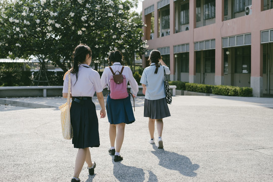 后视图-三个美丽的亚泰学生穿着不同的制服走进学校。