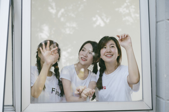 三个穿着白色休闲衬衫的美丽亚泰学生在宿舍楼内的镜子窗前。
