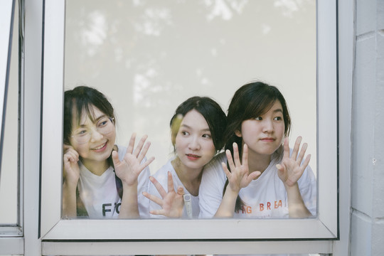 三个穿着白色休闲衬衫的美丽亚泰学生在宿舍楼内的镜子窗前。