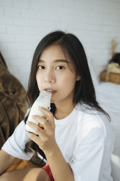 可爱的亚洲年轻女子早餐在卧室喝牛奶。