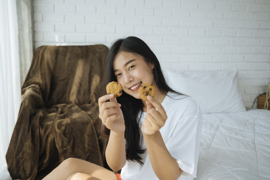 卧室里的泰国女人拿着两块饼干微笑着。