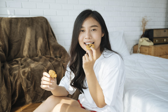 可爱的泰国女孩在卧室吃饼干当早餐。
