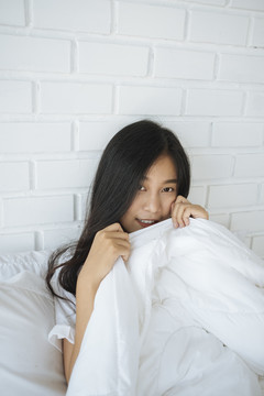 可爱的亚洲女人躲在卧室的白色毯子下。