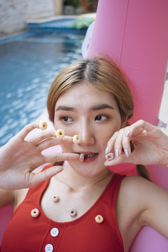 身着红色比基尼的泰国美女躺在粉色泳衣上，在游泳池里享用点心。