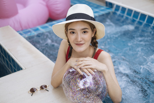 穿着红色比基尼，戴着帽子的泰国美女，喜欢在游泳池里玩透明的闪光球。