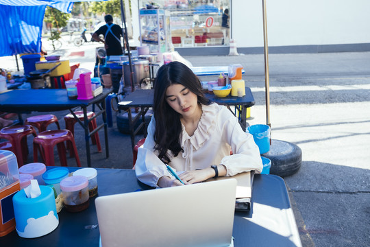 穿着休闲衬衫在户外街头小吃摊工作的泰国美女。