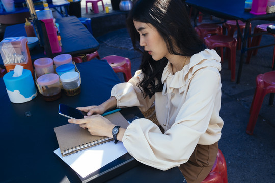 穿着休闲衬衫，在户外工作的泰国漂亮女商人用智能手机在网上联系人们。