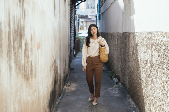 时尚写真-穿着休闲衬衫的泰国职业女商人手持篮子在街巷散步。