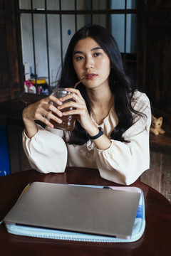 穿着休闲衬衫在家里用吸管喝可乐的泰国职业女商人的特写镜头。