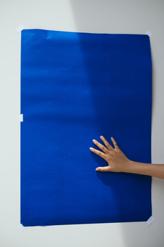 女人的手把蓝色的纸放在墙上，有光有影。